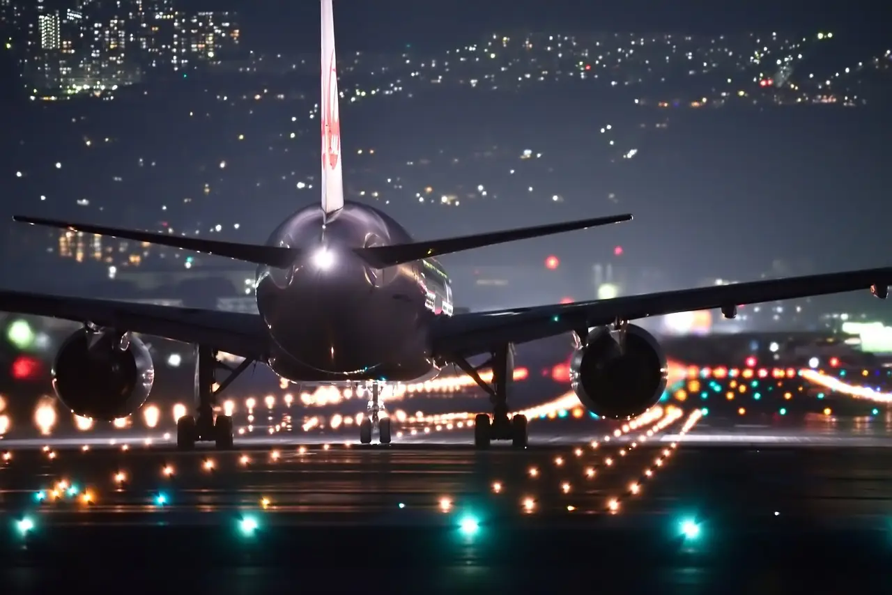 Airplane on runway at night with lights and city skyline in background.